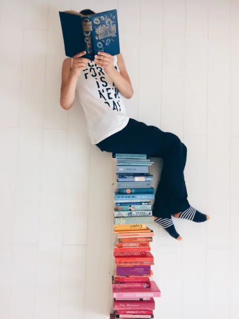 A person sitting on a stack of books, reading