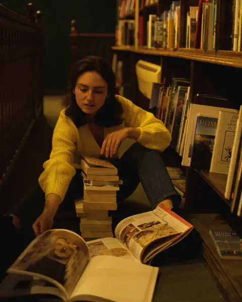 A woman sitting on the floor of a library browsing through books