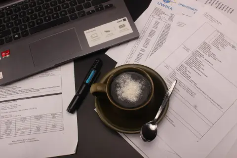 A warm cup of coffee on a desk beside study materials