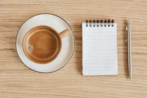 A flat lay of coffee and a notebook with a pen