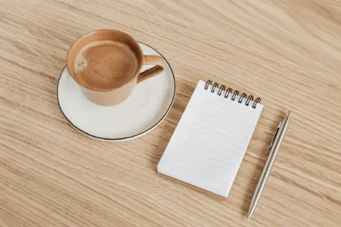 A wooden table with coffee and an open notebook with a pen