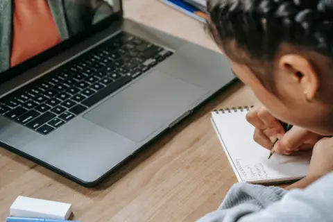 A student studying with a laptop and writing notes
